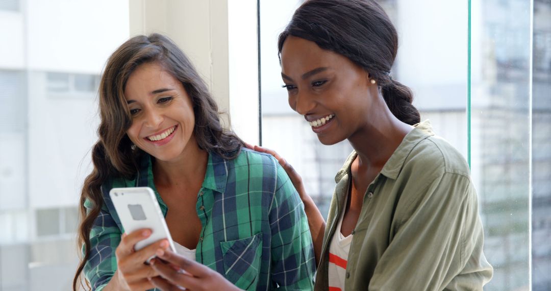 Two Friends Smiling and Looking at Smartphone While Sharing Moment Together - Free Images, Stock Photos and Pictures on Pikwizard.com