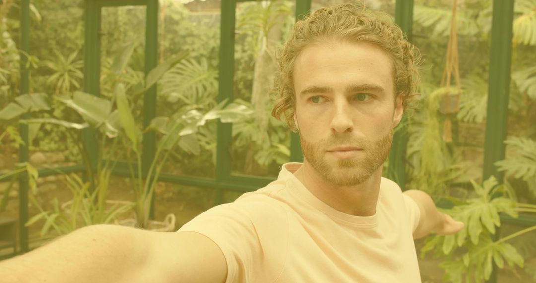 Man standing in greenhouse reaching toward tropical plants exploring sunlit conservatory