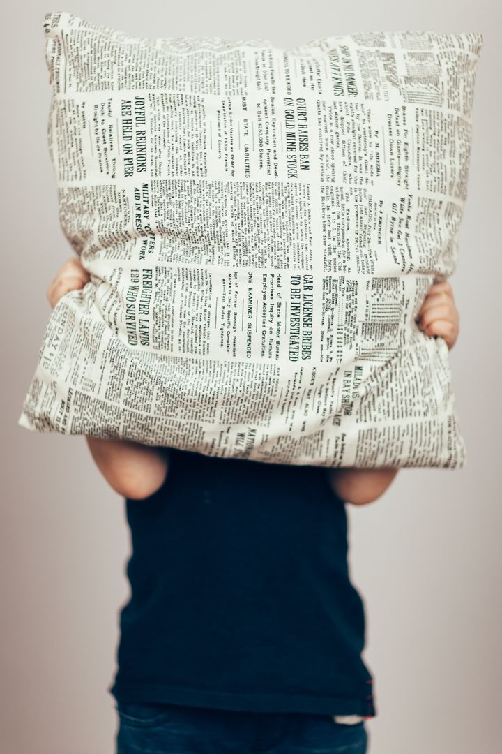 Child Hiding Face with Newspaper Print Pillow