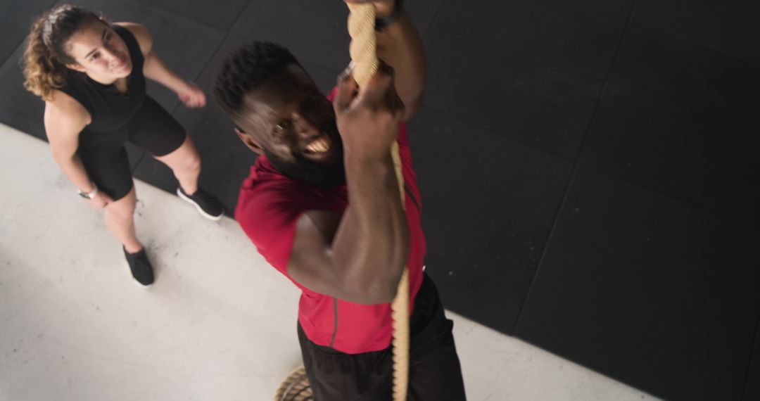 Man Climbing Rope with Spotter in Modern Gym