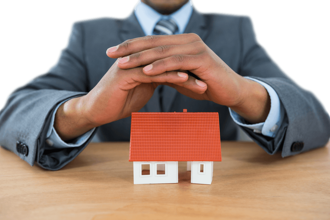 Businessman Covering Small House Model with Hands on Table Transparent Background