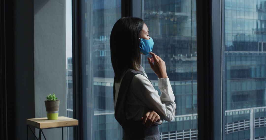 Professional Woman in Blue Face Mask Looking Out Office Window - Free Images, Stock Photos and Pictures on Pikwizard.com