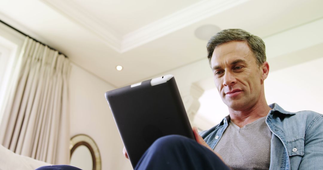 Middle-aged Man Reading on Tablet in Cozy Living Room - Free Images, Stock Photos and Pictures on Pikwizard.com