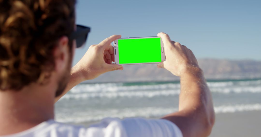 Man Holding Smartphone with Green Screen on Beach - Free Images, Stock Photos and Pictures on Pikwizard.com