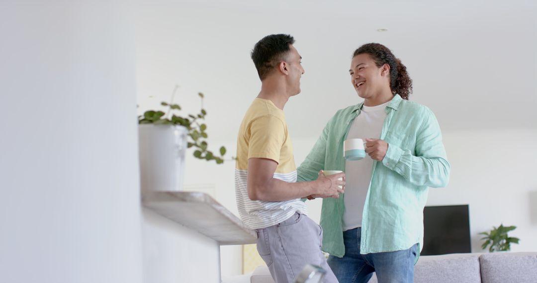 Two men smiling and chatting while holding coffee cups in modern living room - Free Images, Stock Photos and Pictures on Pikwizard.com