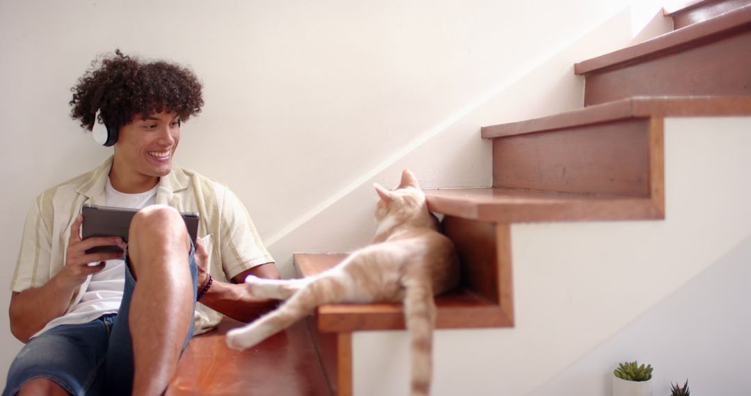 Man Enjoying Technology and Music Next to Relaxing Cat on Staircase