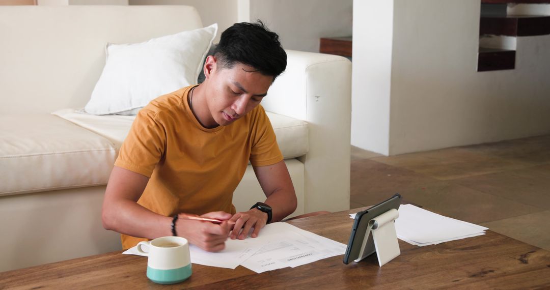 Man Writing on Paper Using Tablet Adapting Creative Home Workspace