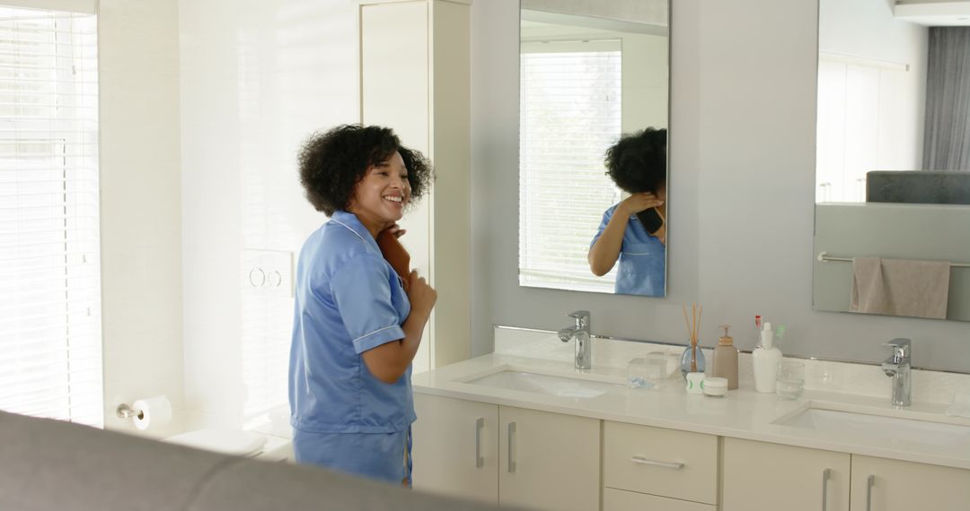 Healthcare worker unwinding after shift smiling while holding towel at bathroom vanity