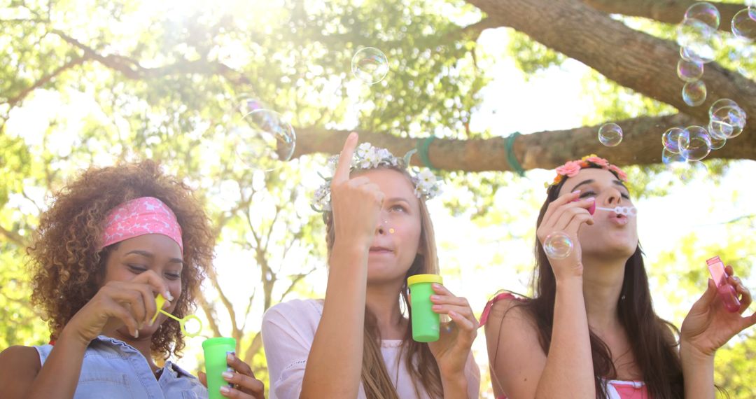 Young Women Blowing Bubbles in Sunlit Park - Free Images, Stock Photos and Pictures on Pikwizard.com