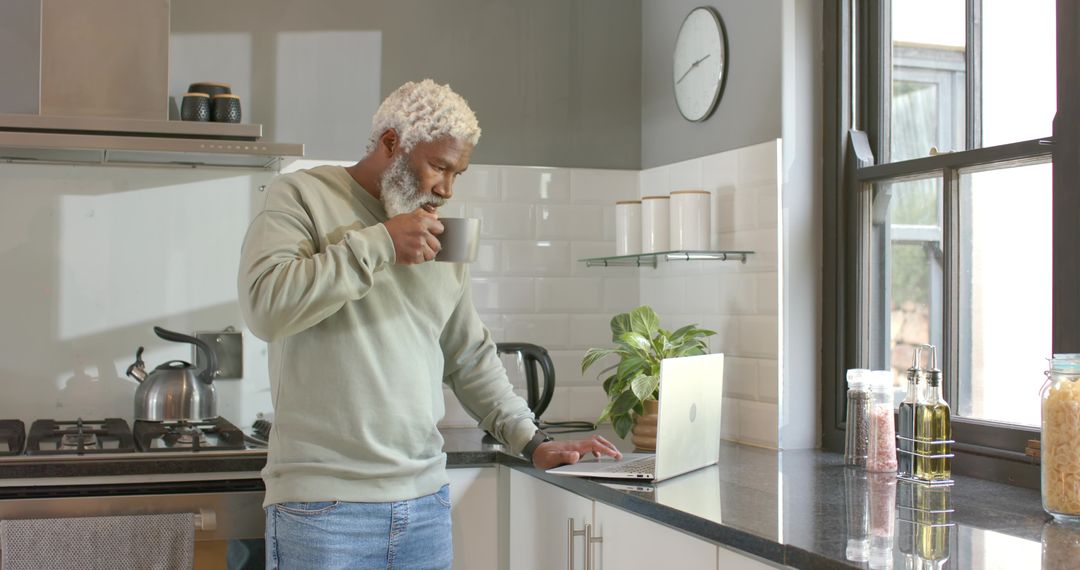 Elderly Man Relaxing at Home with Coffee Using Laptop in Modern Kitchen