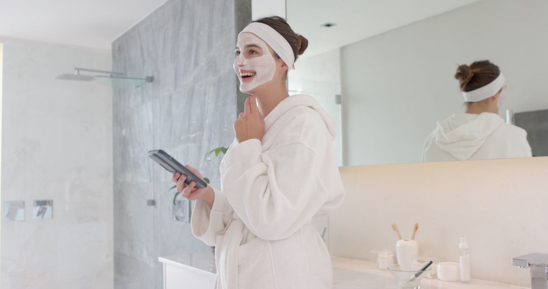 Joyful Woman in Bathrobe Enjoys Skincare Routine Looking at Smartphone