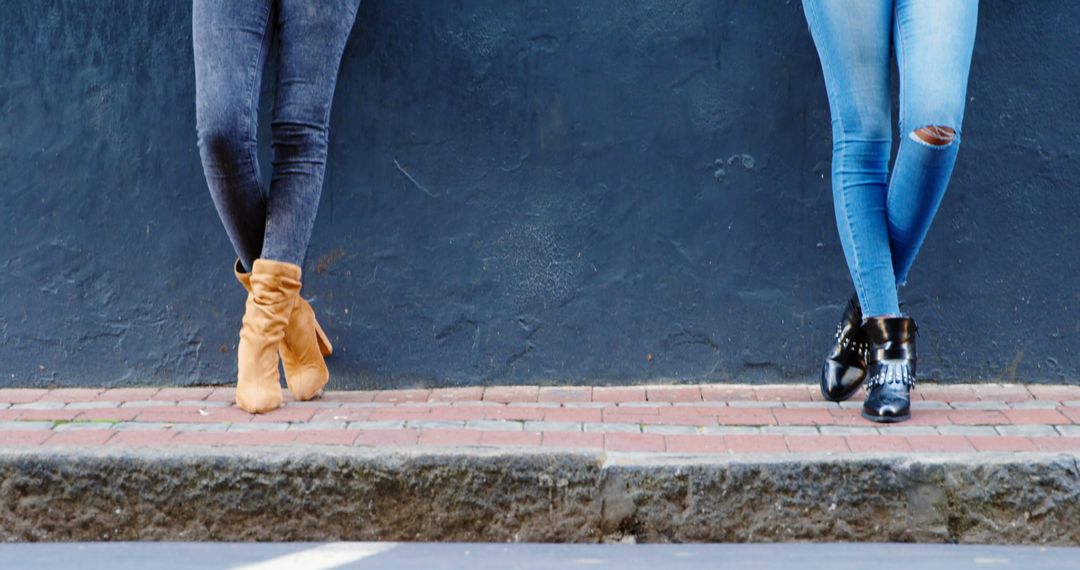 Stylish Twin Sisters Using Smartphones While Leaning Against Urban Wall