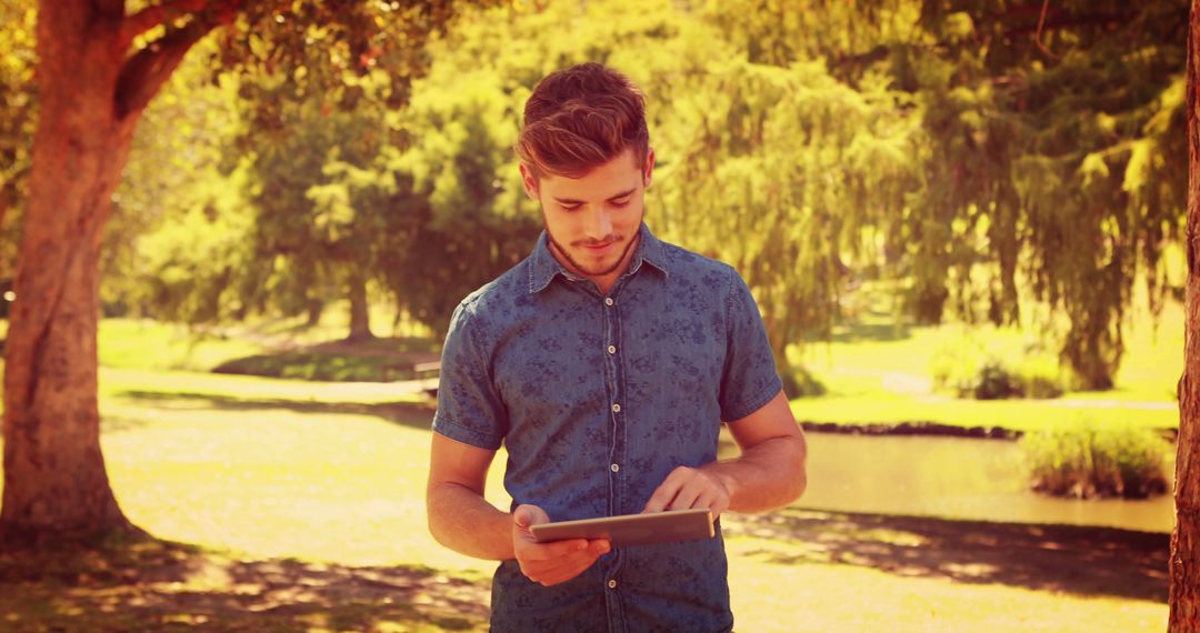 Young Man Using Digital Tablet in Park on Sunny Day - Free Images, Stock Photos and Pictures on Pikwizard.com