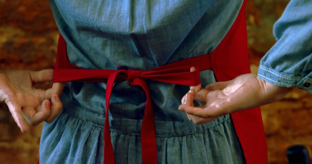 Close-up of hands tying red apron knot around waist - Free Images, Stock Photos and Pictures on Pikwizard.com