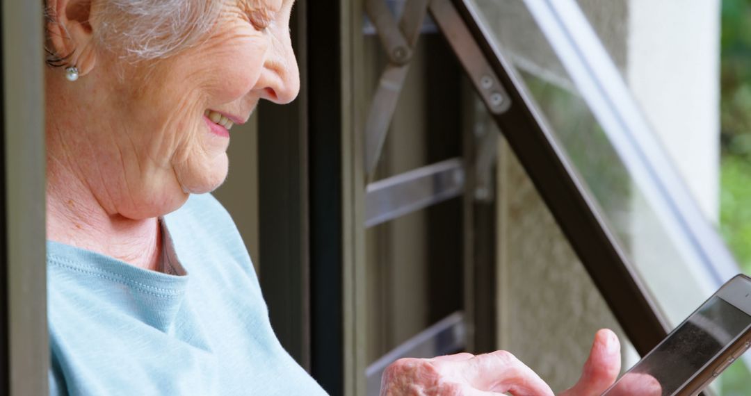 Senior Woman Smiling and Using Smartphone by Window - Free Images, Stock Photos and Pictures on Pikwizard.com