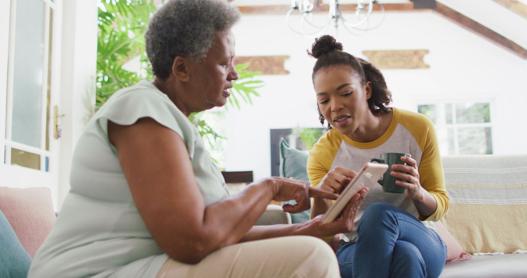 Young Woman Assisting Elderly Woman with Tablet at Home - Free Images, Stock Photos and Pictures on Pikwizard.com