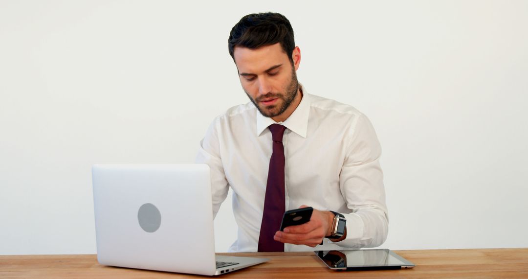 Businessman Multitasking with Phone, Laptop, and Tablet at Office Desk - Free Images, Stock Photos and Pictures on Pikwizard.com