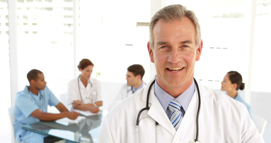 Smiling Senior Doctor with Medical Team Meeting in Background - Free Images, Stock Photos and Pictures on Pikwizard.com