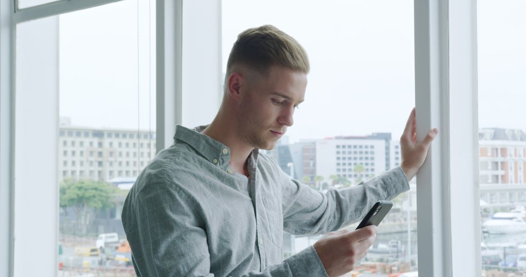 Young Professional Texting on Smartphone by Office Window - Free Images, Stock Photos and Pictures on Pikwizard.com