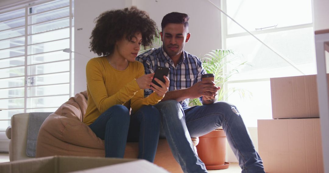 Couple Using Smartphone Arranging New Home Surrounded by Boxes