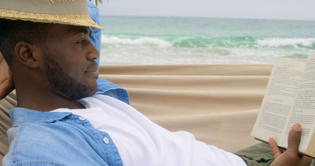 Man Relaxing in Hammock Reading a Book on Beach