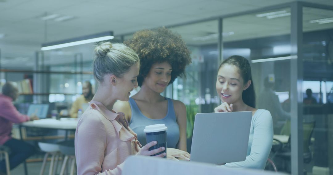 Diverse women collaborating over laptop in modern coworking space with reusable cup