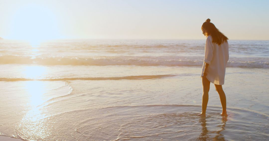 Woman Walking on Sunset Beach with Waves and Bright Sunlight - Free Images, Stock Photos and Pictures on Pikwizard.com