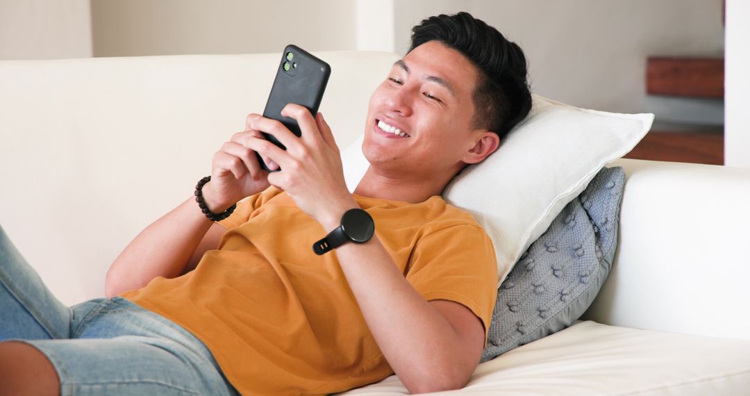 Young Man Relaxing at Home Browsing Smartphone and Checking Smartwatch