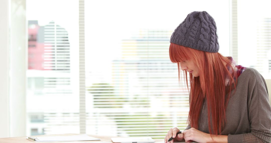A red-haired woman in casual clothes and a beanie is absorbed in her smartphone indoors. - Free Images, Stock Photos and Pictures on Pikwizard.com
