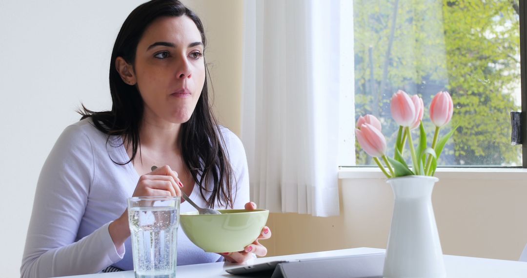 Woman Eating Breakfast Next to a Window with Tulips on Table - Free Images, Stock Photos and Pictures on Pikwizard.com