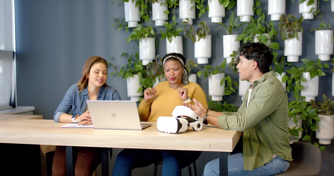 Diverse team collaborating over laptop and VR headset in biophilic modern office
