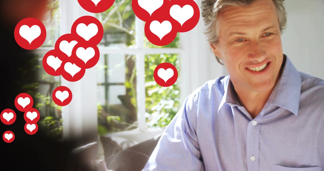 Mature man smiling on sunlit sofa with floating heart icons conveying online affection