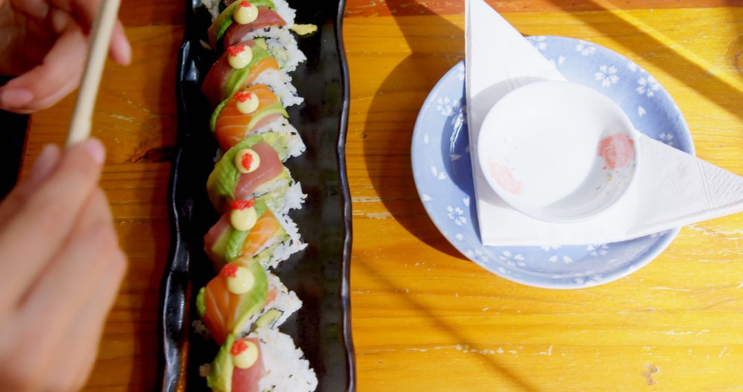 Hand Holding Chopsticks Approaching Sushi Roll on Wooden Table - Free Images, Stock Photos and Pictures on Pikwizard.com