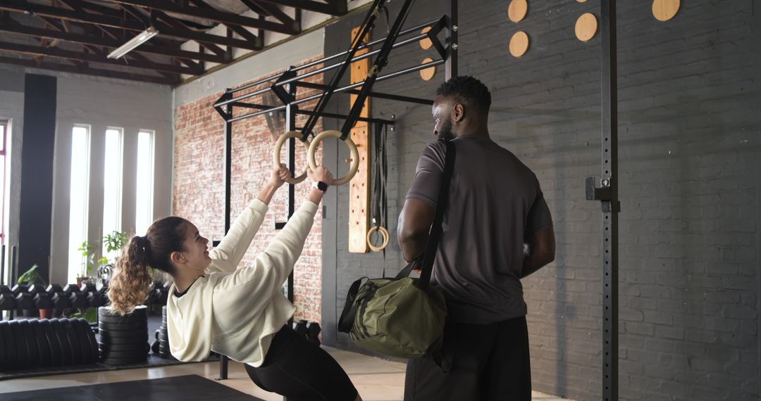 Personal Trainer Assisting Client with Ring Rows in Industrial Gym Setting