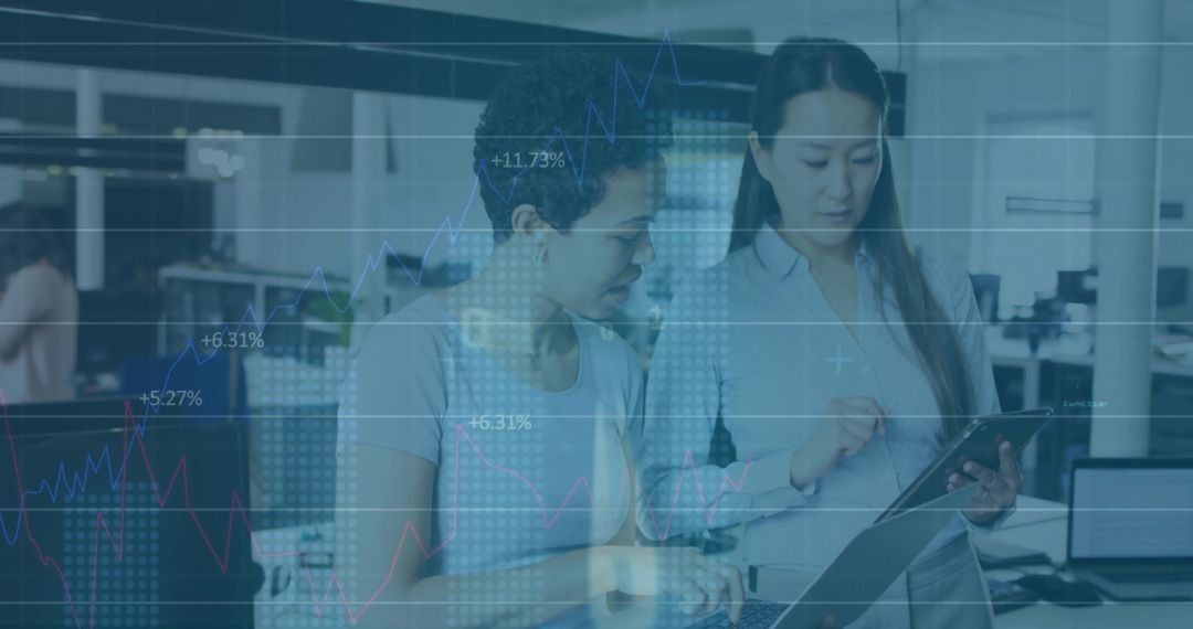 Two Women Collaborating and Analyzing Financial Dashboard on Tablet and Laptop in Open Office