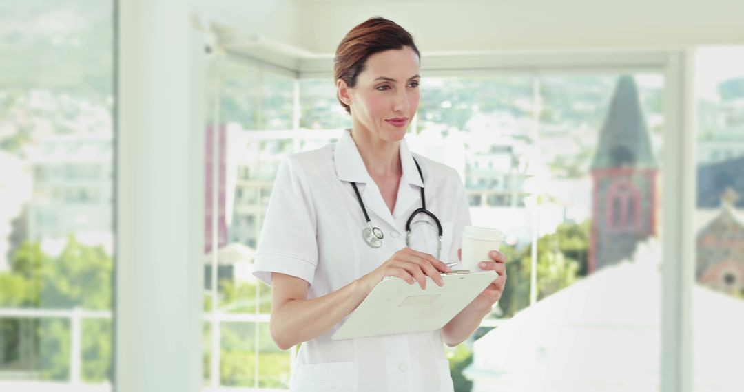 Confident Female Doctor Holding Clipboard and Coffee in Bright Hospital Office - Free Images, Stock Photos and Pictures on Pikwizard.com