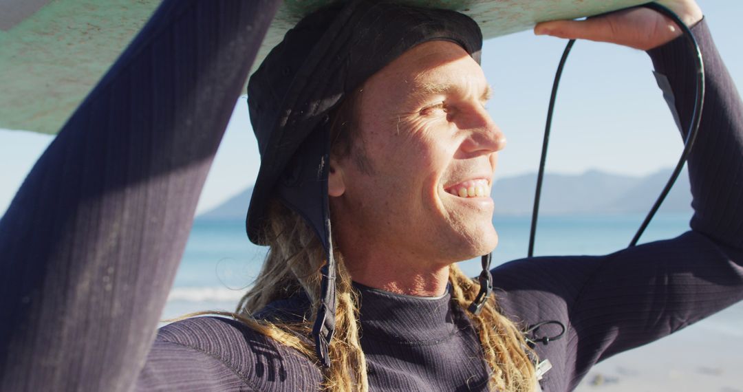 Surfer with long braided hair holding surfboard on sunny beach - Free Images, Stock Photos and Pictures on Pikwizard.com