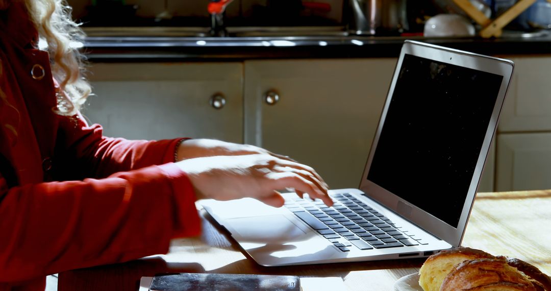 Person working on laptop at home kitchen with breakfast pastries - Free Images, Stock Photos and Pictures on Pikwizard.com