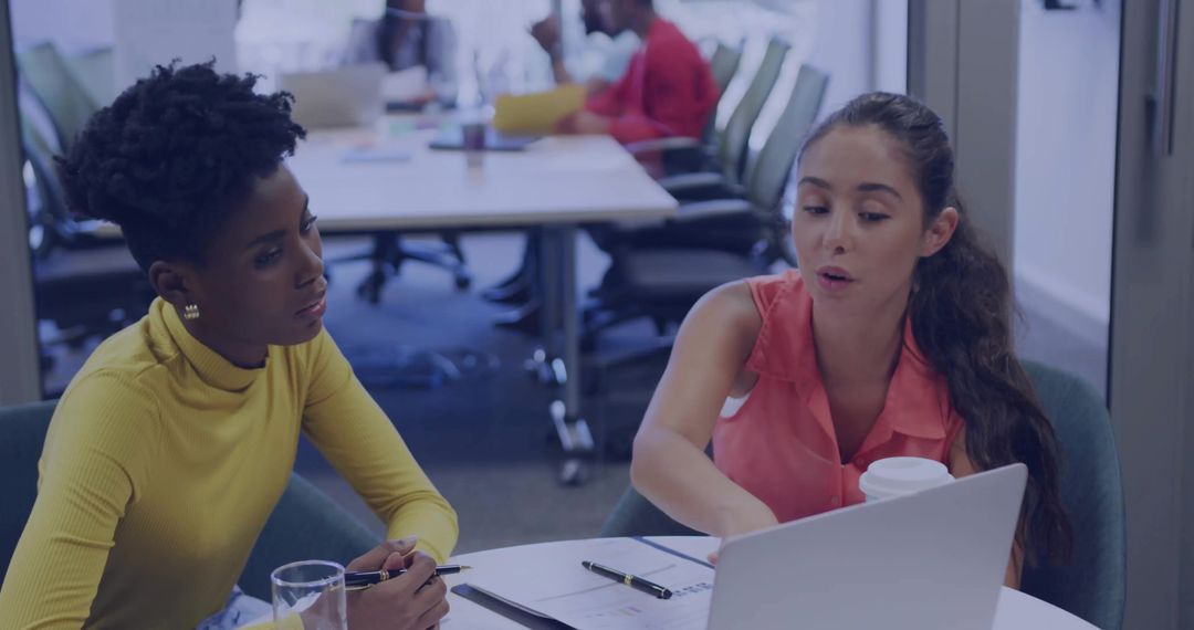 Women Collaborating at Roundtable Meeting Pointing at Laptop with Coffee and Documents