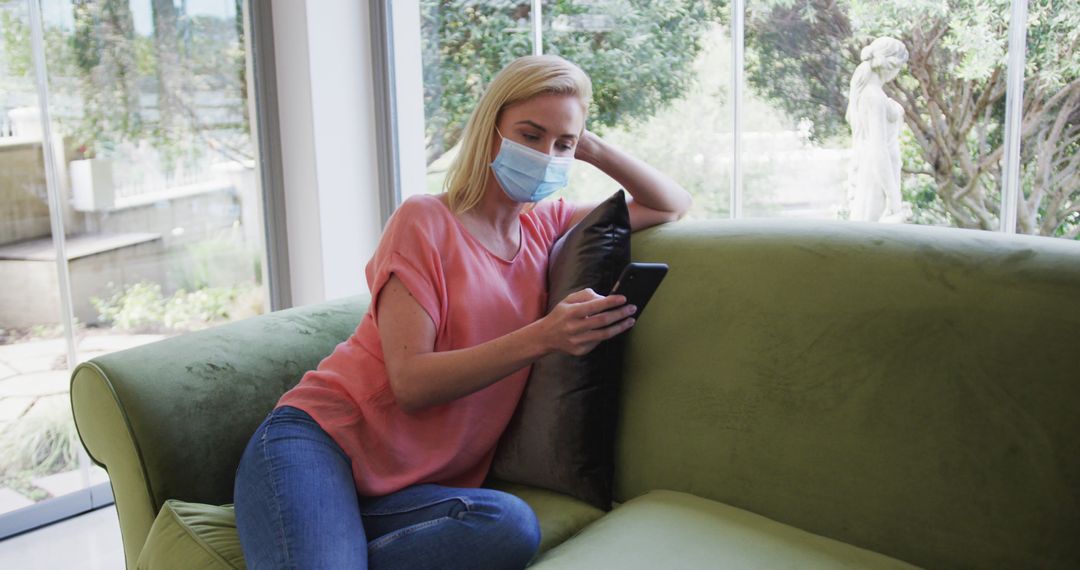 Woman Wearing Mask Relaxing on Couch and Using Smartphone at Home - Free Images, Stock Photos and Pictures on Pikwizard.com