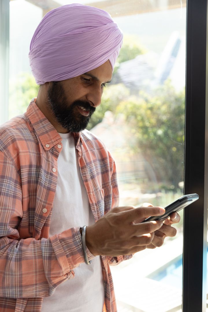Man in Turban Using Smartphone by Glass Door at Home