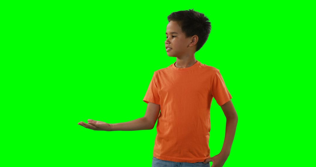 Young Boy in Orange Shirt Gesturing with Open Hand Against Green Background - Free Images, Stock Photos and Pictures on Pikwizard.com