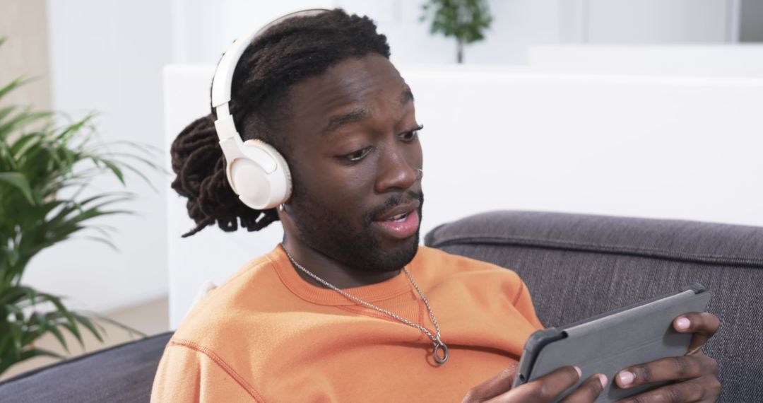 African American man relaxing on couch listening with headphones and using tablet