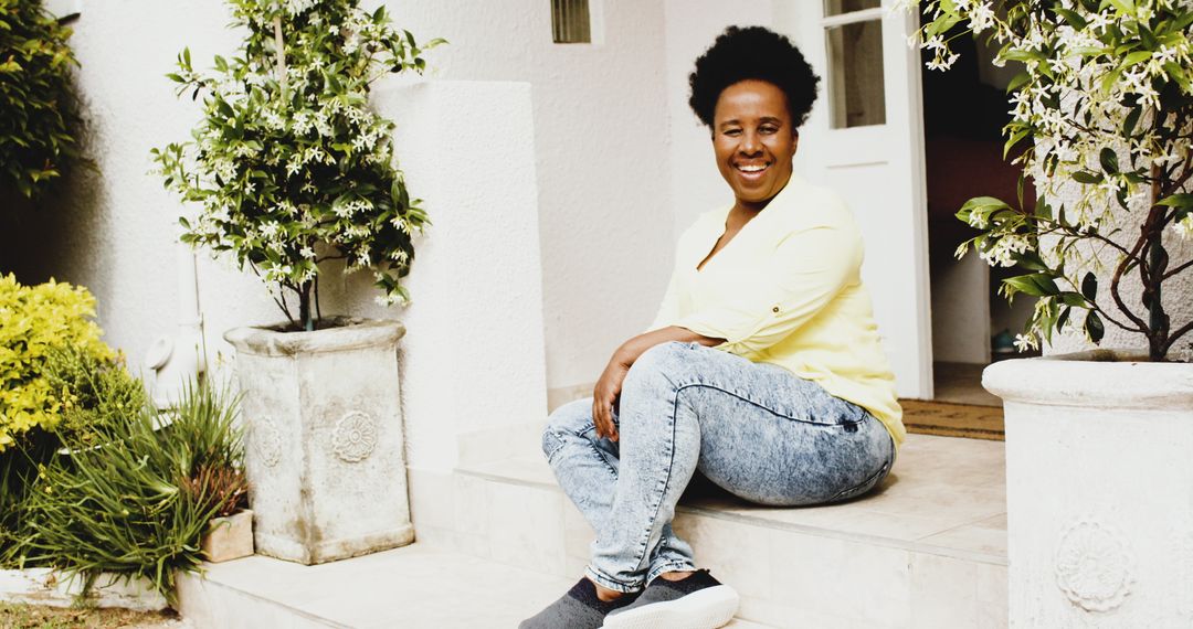 Relaxed African American Woman Sitting on Her Porch with White Walls and Plants - Free Images, Stock Photos and Pictures on Pikwizard.com