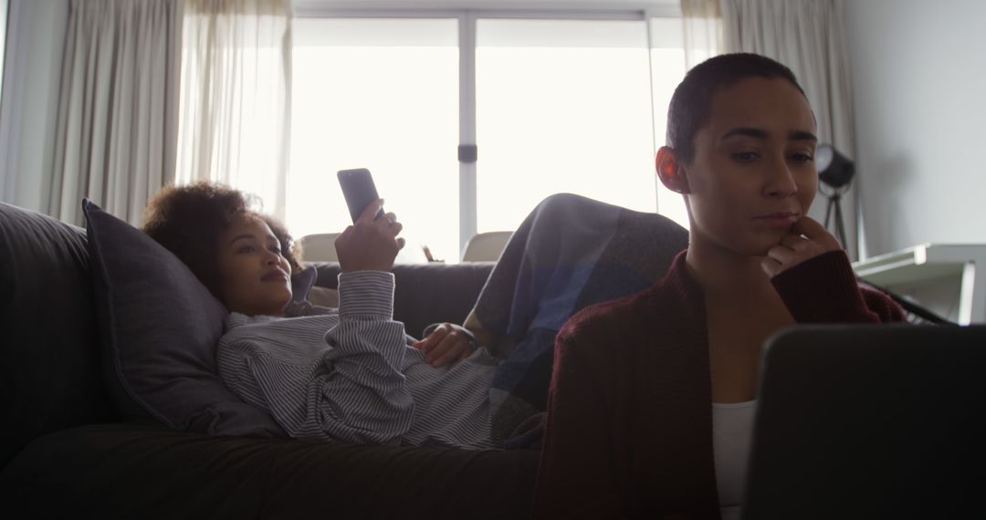 Two Women Relaxing on Couch Using Smartphone and Laptop - Free Images, Stock Photos and Pictures on Pikwizard.com