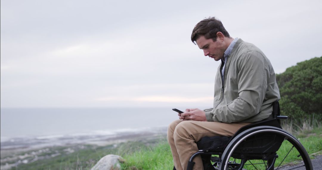 Man in Wheelchair Using Smartphone Outdoors with Ocean View - Free Images, Stock Photos and Pictures on Pikwizard.com