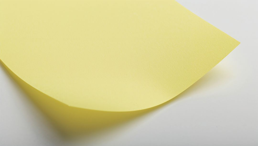Curled Yellow Sticky Note on White Surface with Soft Shadow and Paper Texture