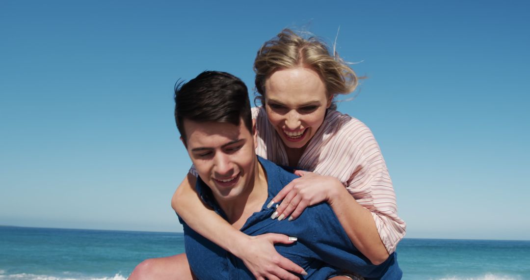 Joyful couple enjoying piggyback ride on beach on a sunny day - Free Images, Stock Photos and Pictures on Pikwizard.com