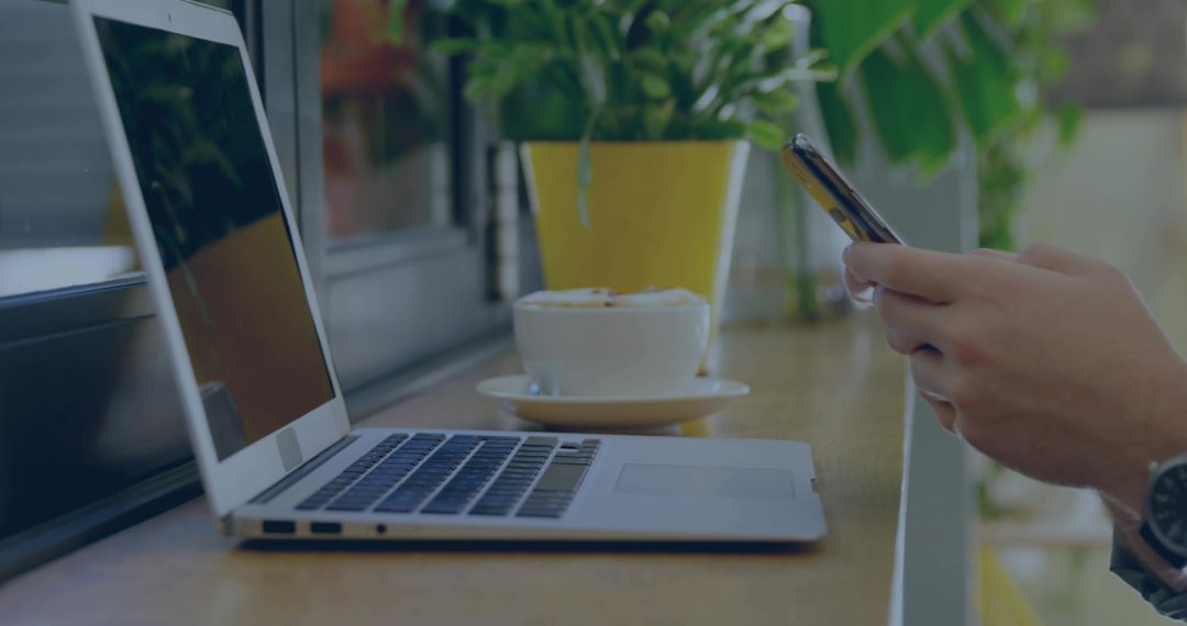 Remote work at cafe counter: man using smartphone and laptop with coffee and plants