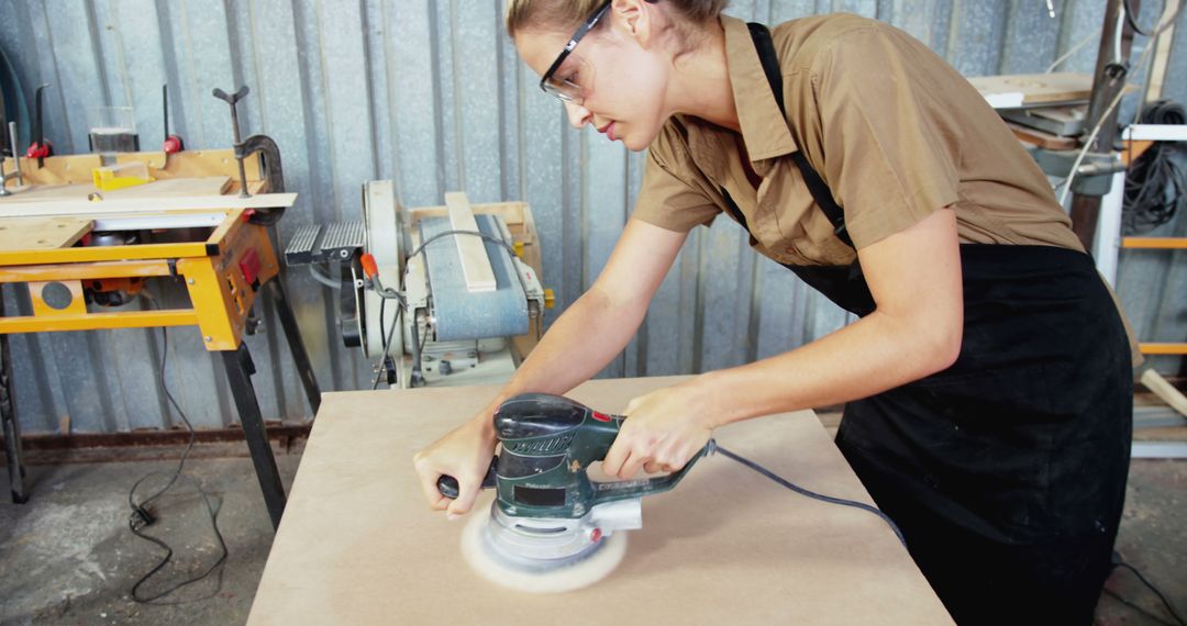 Female Carpenter Wearing Gloves Using Electric Sander on Wooden Board - Free Images, Stock Photos and Pictures on Pikwizard.com